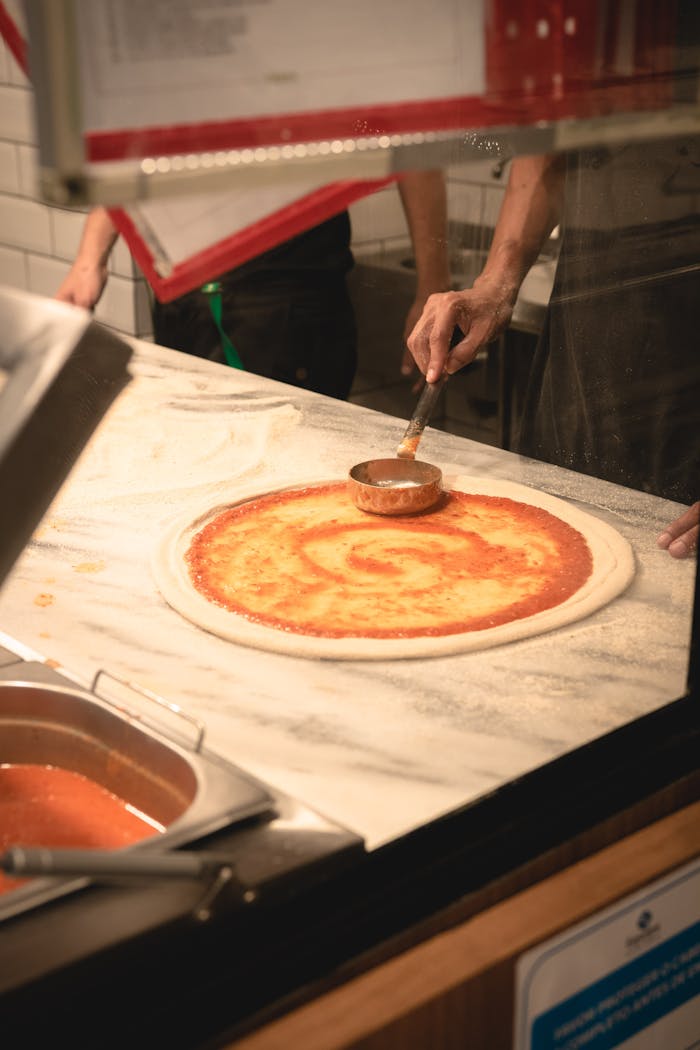 Authentic Italian pizza preparation with fresh tomato sauce on dough in a Brazilian kitchen.